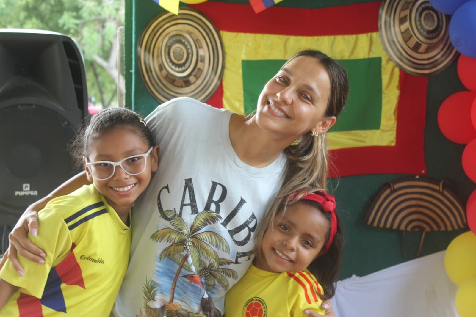 A volunteer with two students in front of the Colombian flag backdrop